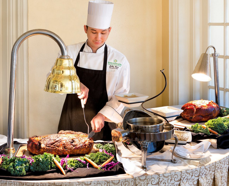 A chef cutting a slab of meat at a buffet table