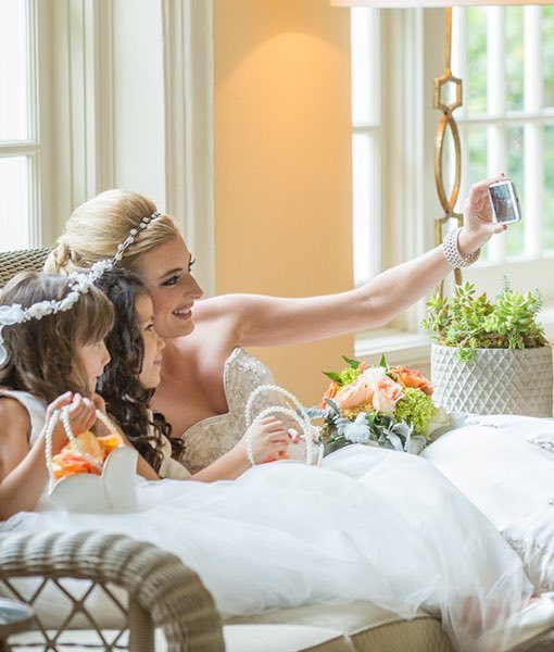 A bride sitting on a couch with her two flower girls taking a selfie