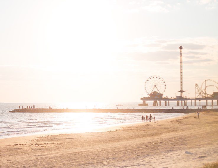 A view of the pier rides from the beach with the sun gleaming on the horizon in the distance