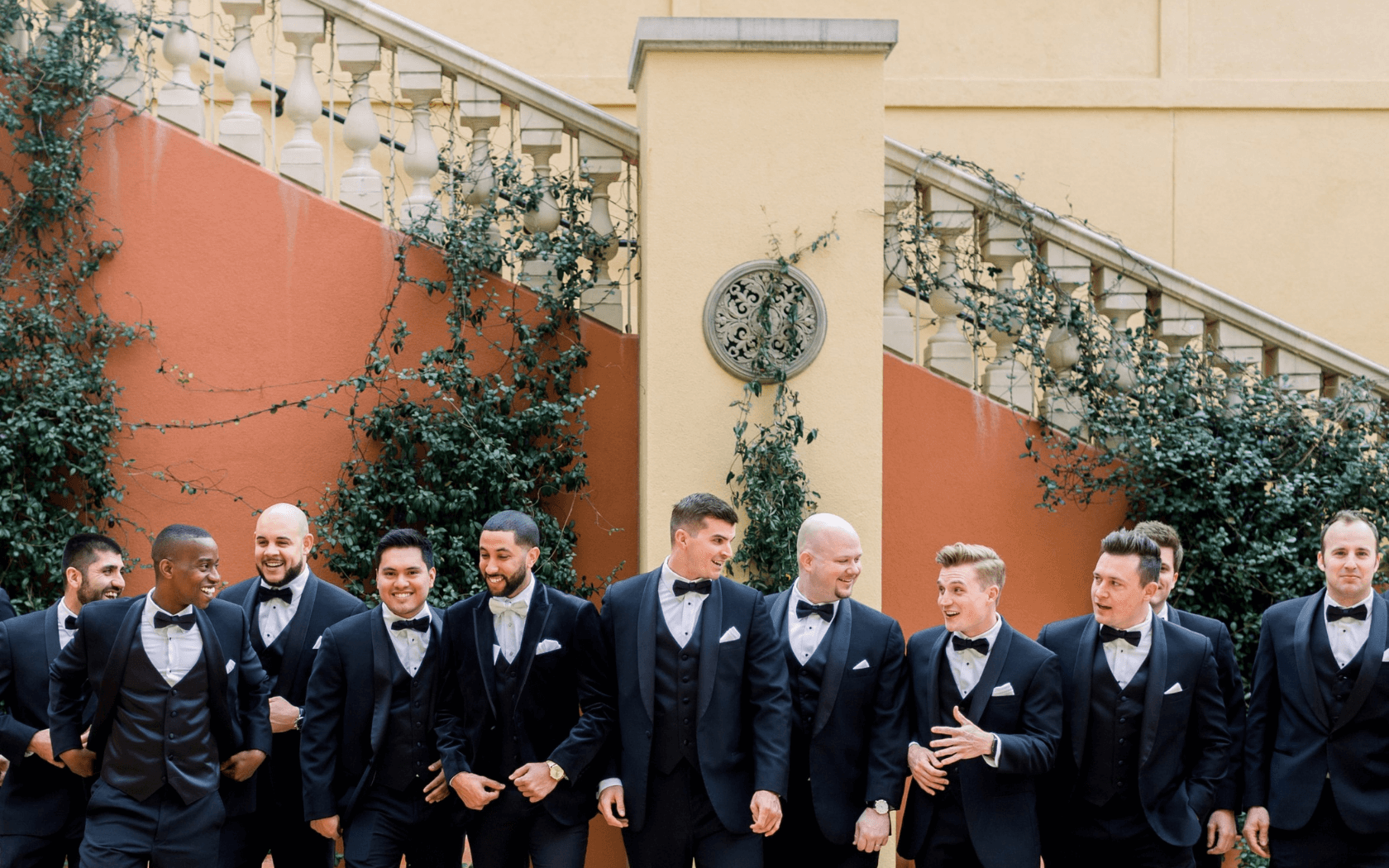 groomsmen lined up in tuxedos in front of staircase in courtyard