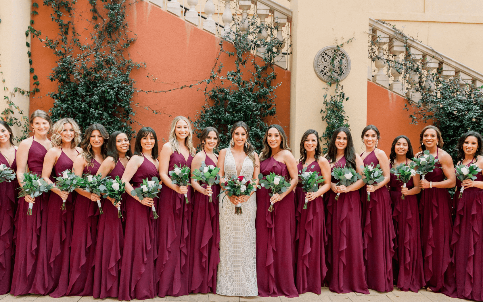 bride and bridesmaids wearing burgundy dresses lined up in front of outside hotel stairs