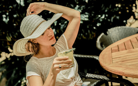 lady holding a fresh lemonade outside on a sunny day with a large hat over her head