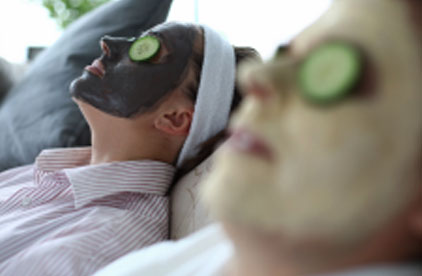 Two woman wearing face masks and cucumber slices on their eyes 
