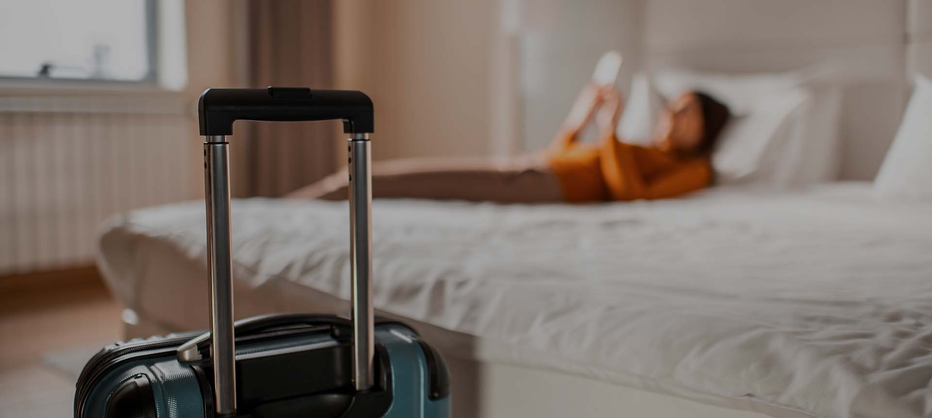 Suitcase in front of a bed where a woman is laying down 