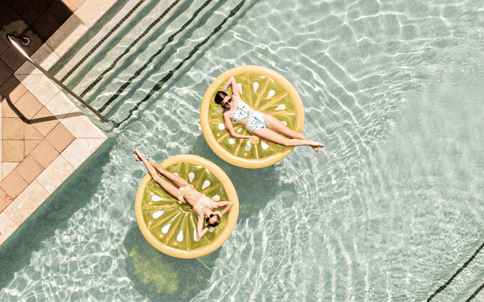 two ladies floating on two lemon-looking floats at the pool