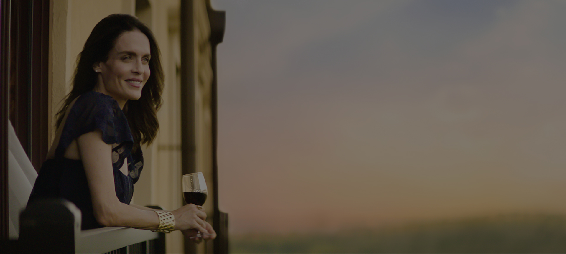 girl looking over her balcony with a glass of wine in her hands