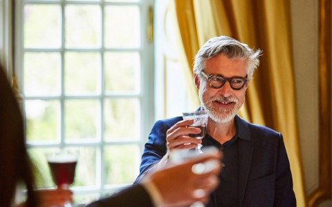 man wearing glasses cheering with a glass of wine