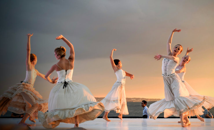 Five female ballet dancers in white dresses dancing on outdoor stage