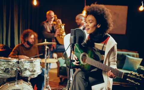 View of a woman and her band on a recording studio singing and playing guitar