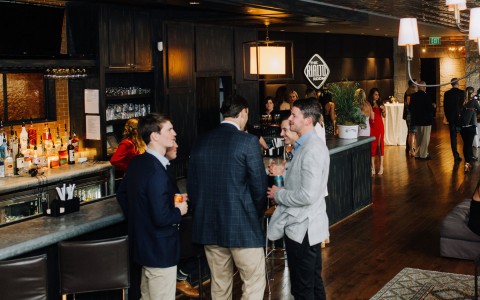 Group of people standing up gathered chatting in a bar 