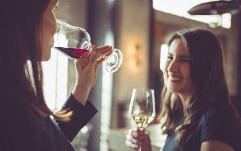 Two woman talking and one of them is holding a glass of wine while the other one takes a sip 