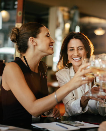 Two women laughing while they are toasting with wine