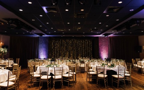 indoor venue set up for a wedding reception with banquet tables and string lights near a wall