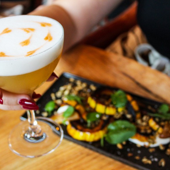 person holding a foamy cocktail and a plate of appetizers