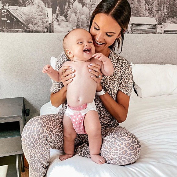 woman in cheetah print pajama set holding smiling baby on bed