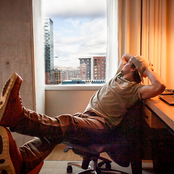 man lounging on office chair in suite and looking out through large window with views of downtown denver