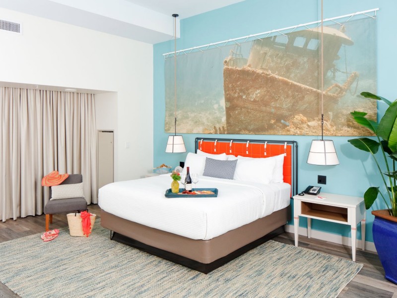 a king bed with a teal wall and painting of a ship