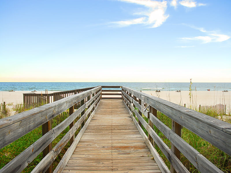 wooden walking path leading to beach on a clear day with blue sky