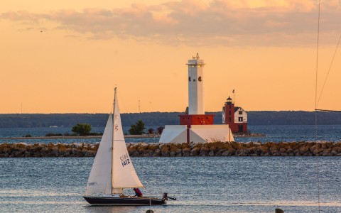 view of a sailboat in front of a lighthouse on a rocky barrier