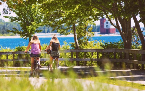 2 women biking down a paved road with a view of the water