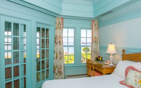 hotel bedroom with baby blue walls, desk and a view of the water