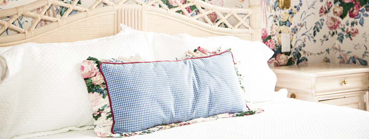 pale blue pillow on white bed in room with floral wallpaper