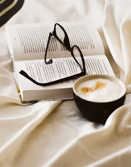 reading glasses sitting on open book next to cup of coffee