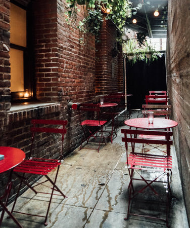 outdoor seating with red tables and chairs next to brick walls