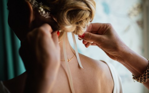 closeup of women tying a head piece on a bride 