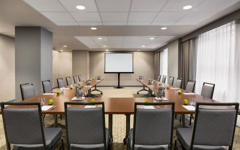 meeting room set up with table and chairs facing a screen 