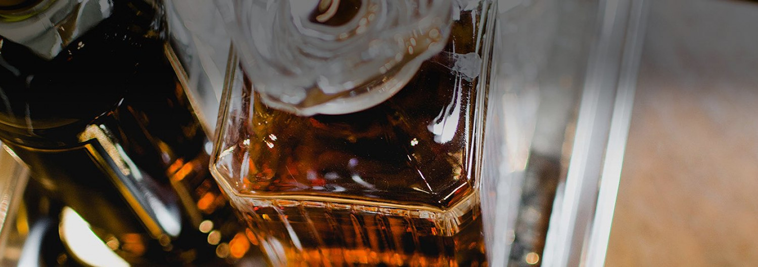 close up of a dark whiskey in a glass decanter on a silver tray