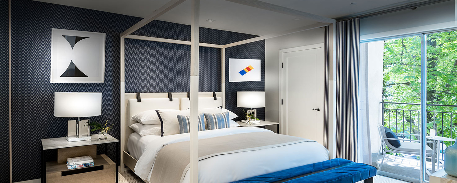 bedroom with a patterned blue wall, white linen bed in a white bed frame, blue bench, and two nightstands with lamps