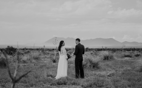 couple standing up in the middle of a field with the mountains in the background 