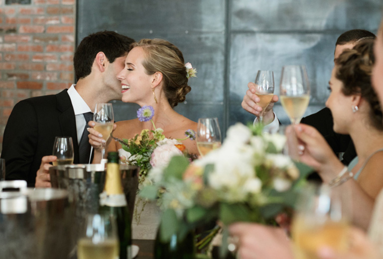 groom kissing the brides cheek while holding a glass of champagne