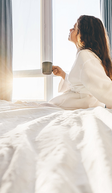 woman wearing a hotel robe with a cup of coffee by the window 