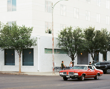 a white building with a red car passing by 