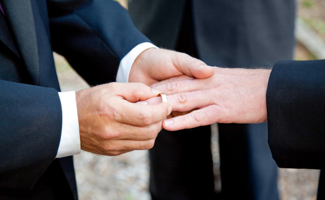 Close up of man placing a wedding band on another man's ring finger