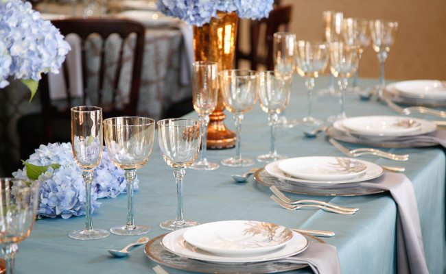 Event table with light blue tablecloth, empty glasses, and plates setup for event