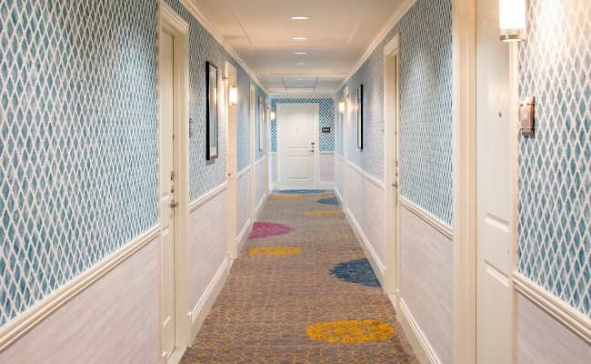 View of hotel rooms hallway with blue tiled walls and carpet with yellow blue and pink circles