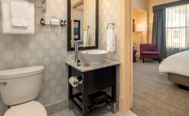View of bathroom with toilet, small sink vanity, mirror, towels, and partial view of accommodation
