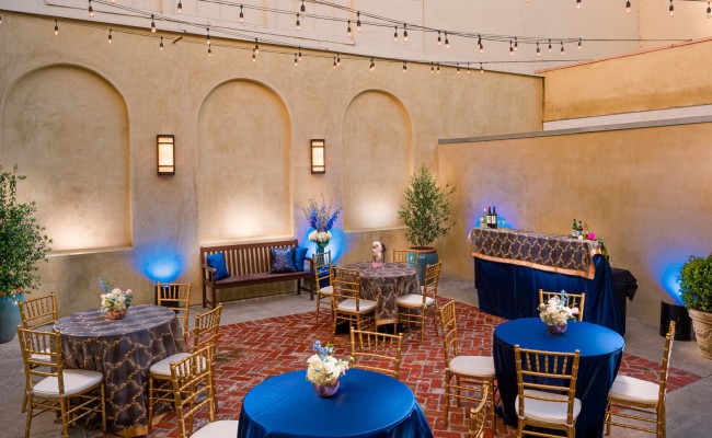 Wedding venue setup with blue tablecloth round tables and gold chairs