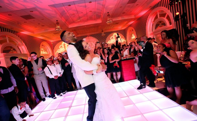 Bride and groom laughing on the dance floor at a wedding surrounded by guests