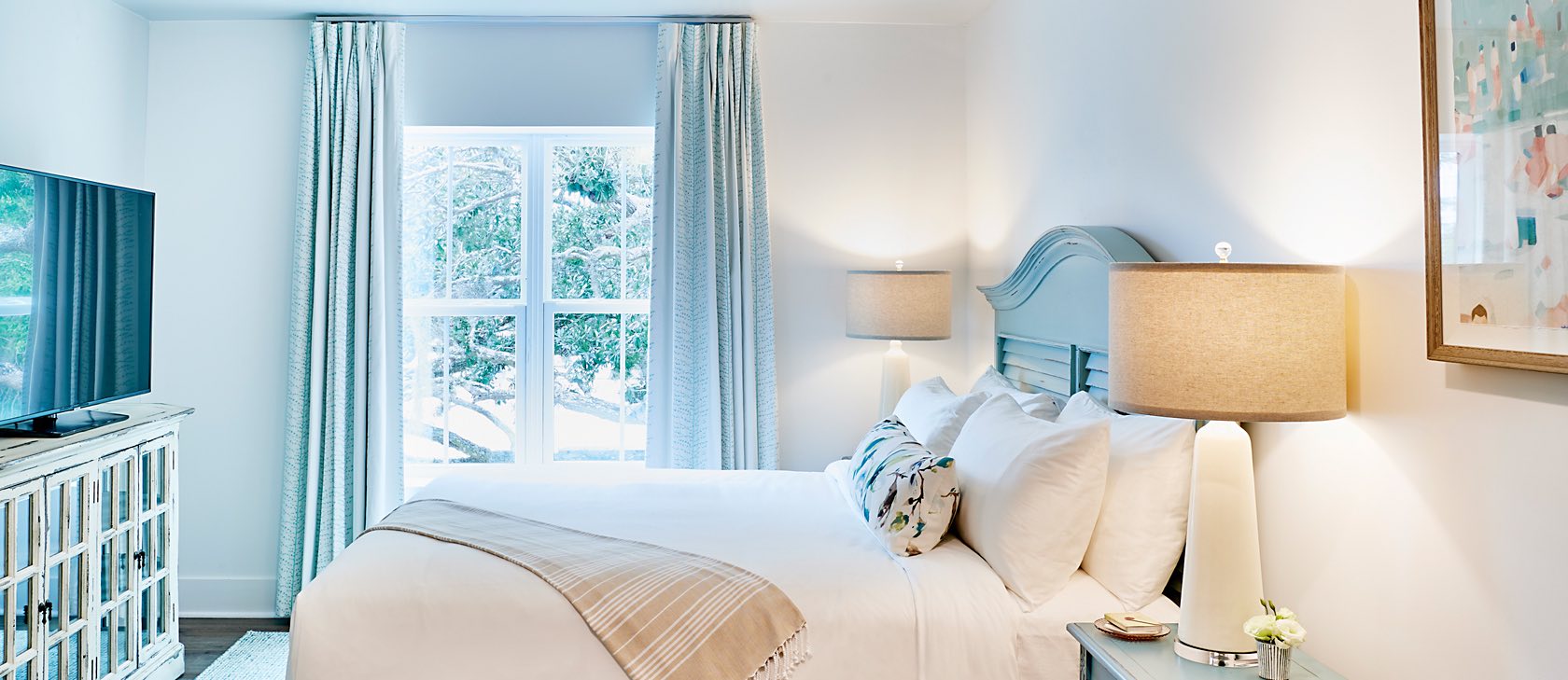 hotel room with natural lighting, a large window and a queen bed with nightstand on each side of the bed