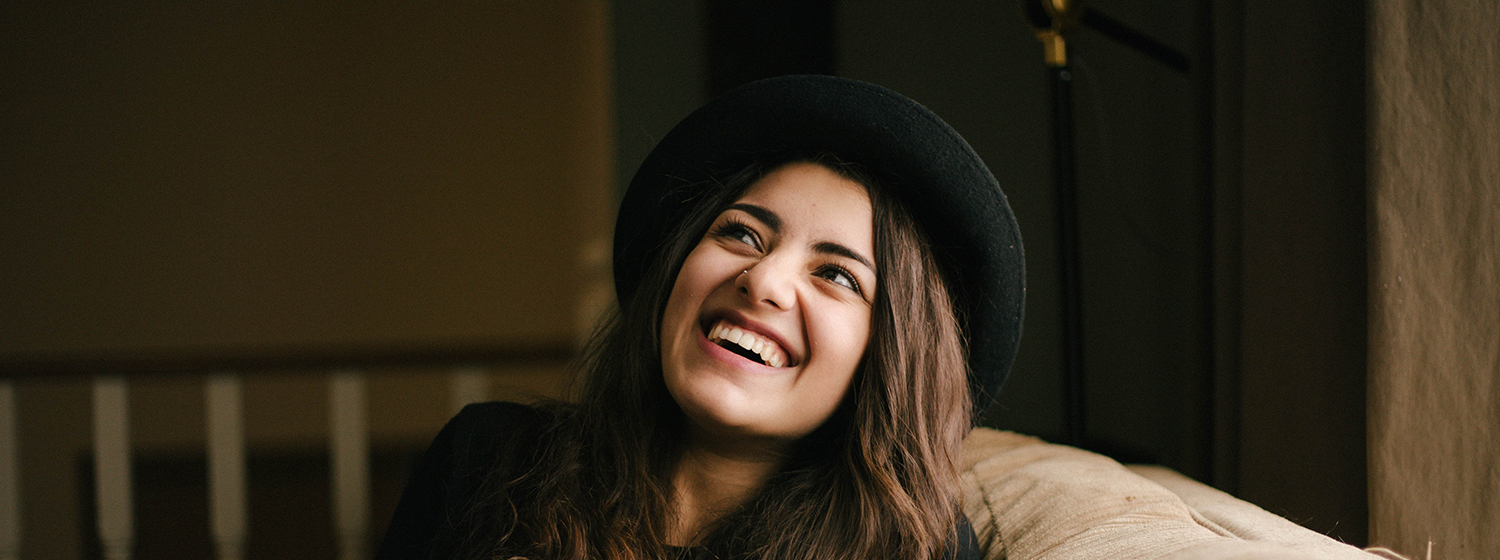Closeup angle of a young woman wearing a hat sitting and laughing while she is looking up 