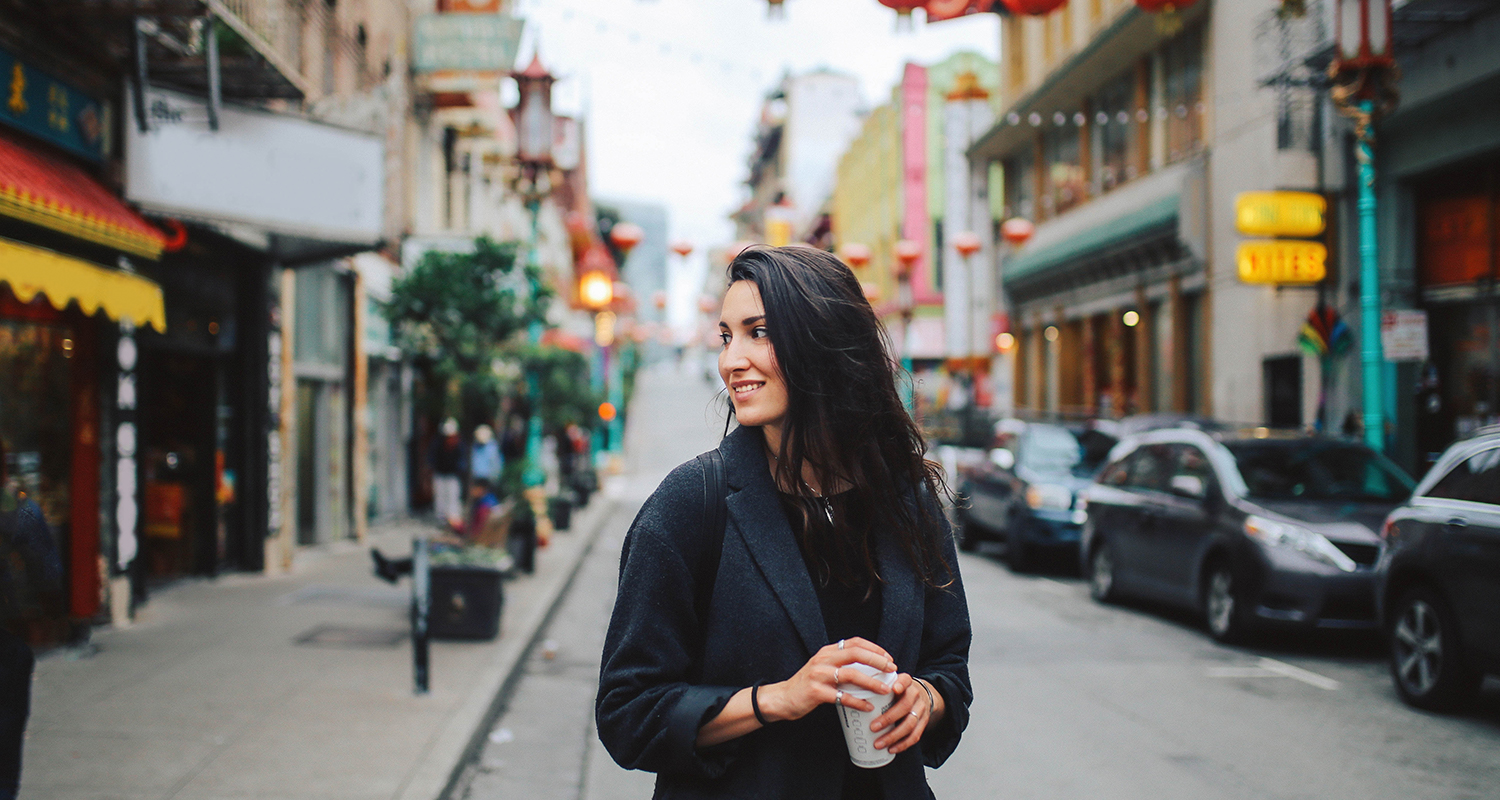 Young woman dressed in black walking in the street holds  is looking and smiling to the left