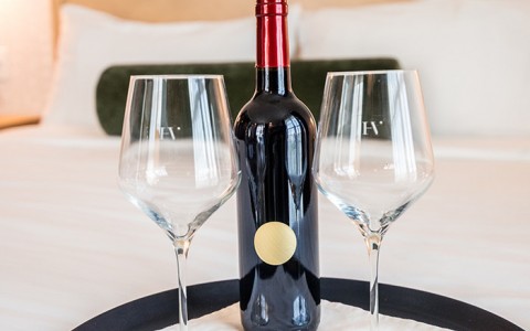 two wine glasses and bottle of red wine on queen size bed