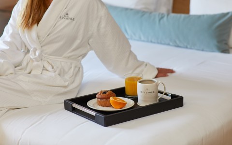 woman wearing white robe sitting on white bed with breakfast food