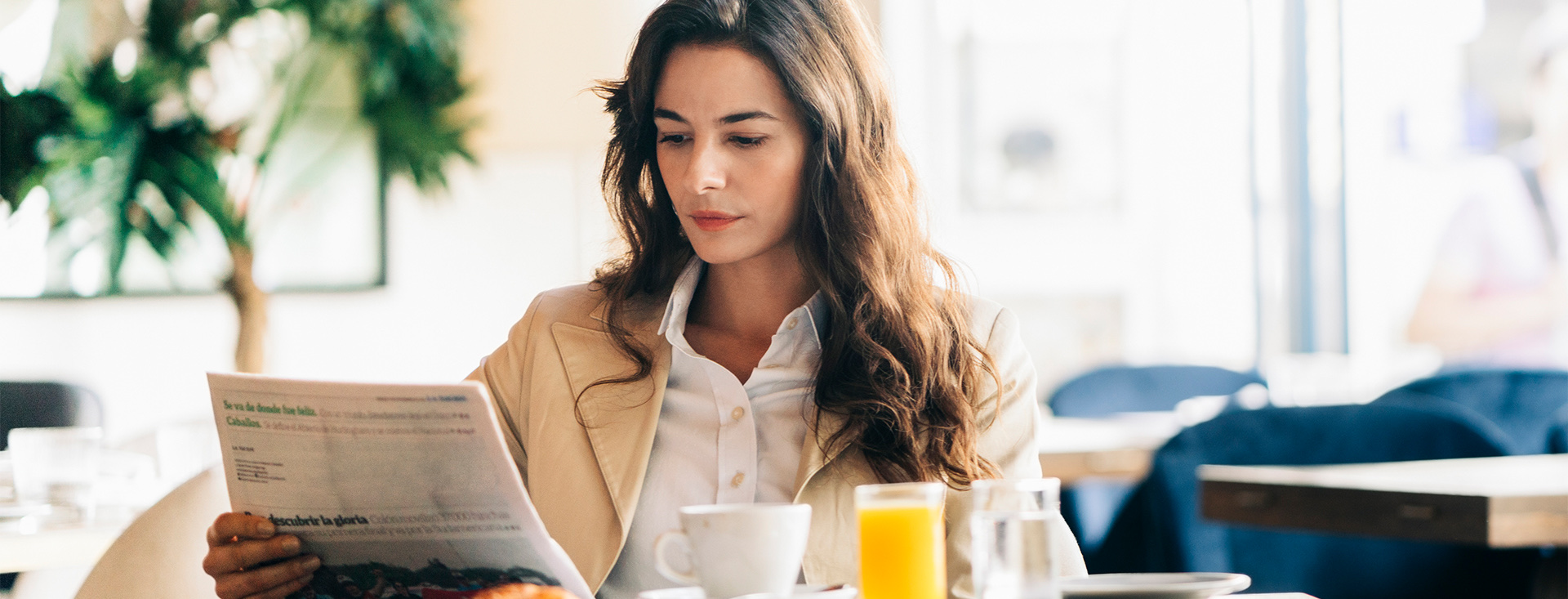 a woman reading a newspaper with a cup of coffee and a glass of orange juice in front of her