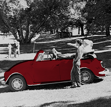 people sitting in a red volkswagen bug outside in a yard