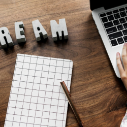 Half a laptop graph paper and dream in block letters on a brown desk